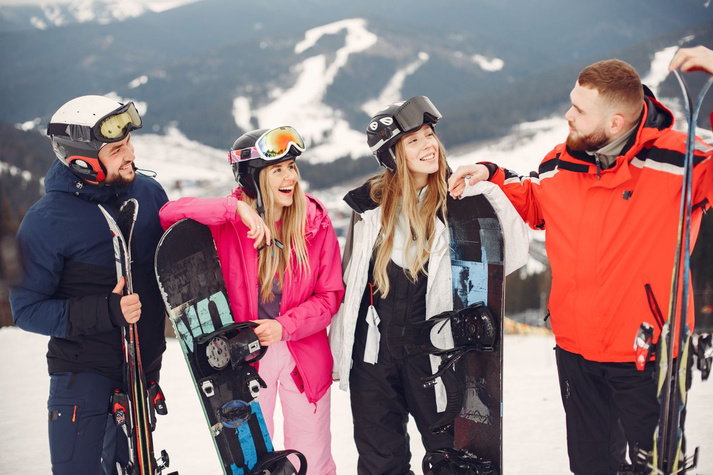 Four friends standing together on a mountain with skis and snowboards